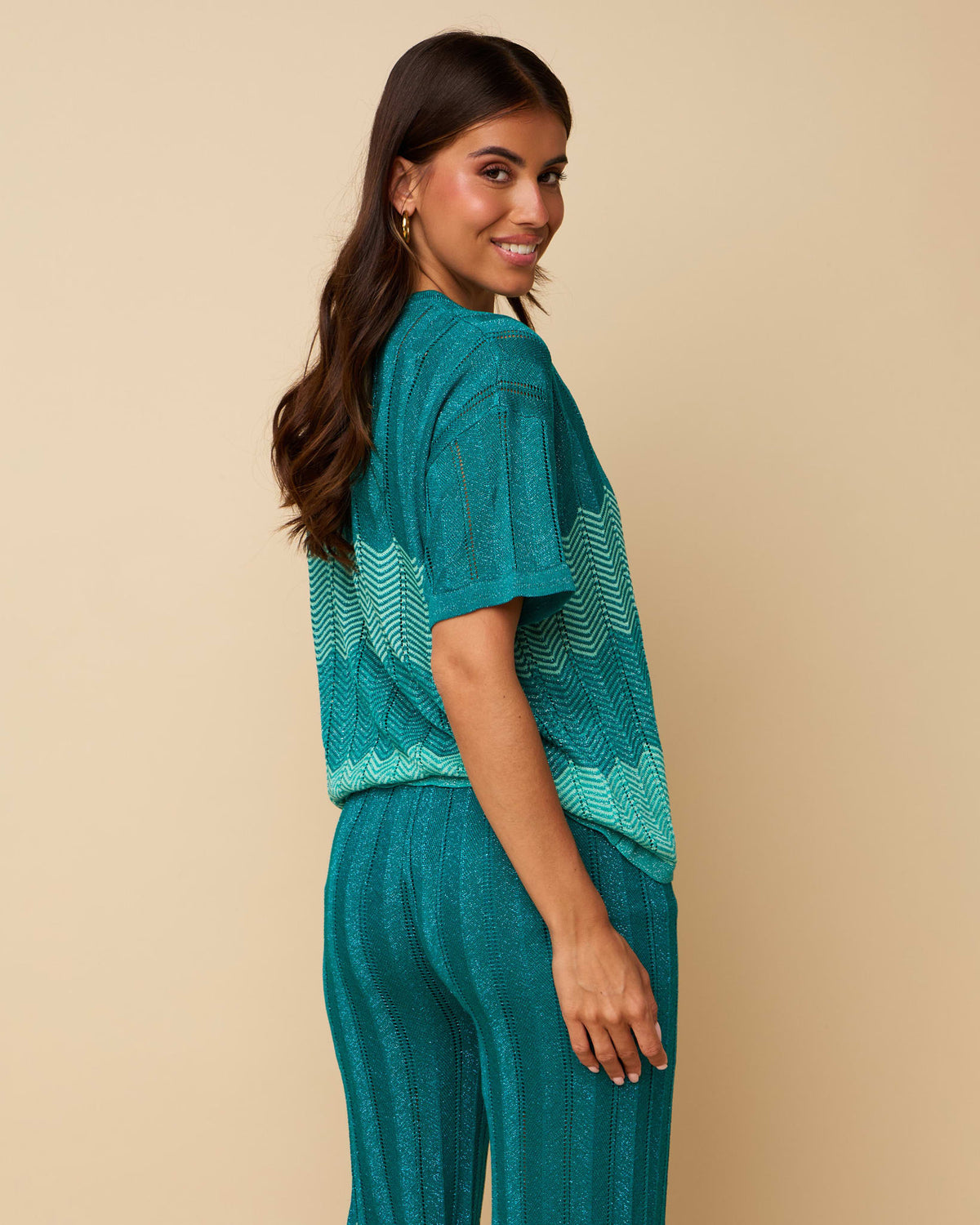 A smiling model poses in HEYB_23_627619, a matching teal knit short-sleeve top and pants set with chevron patterns.