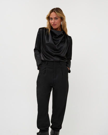 A model poses in a black cowl-neck satin top and pleated trousers, reference 264-15-1-3-18.