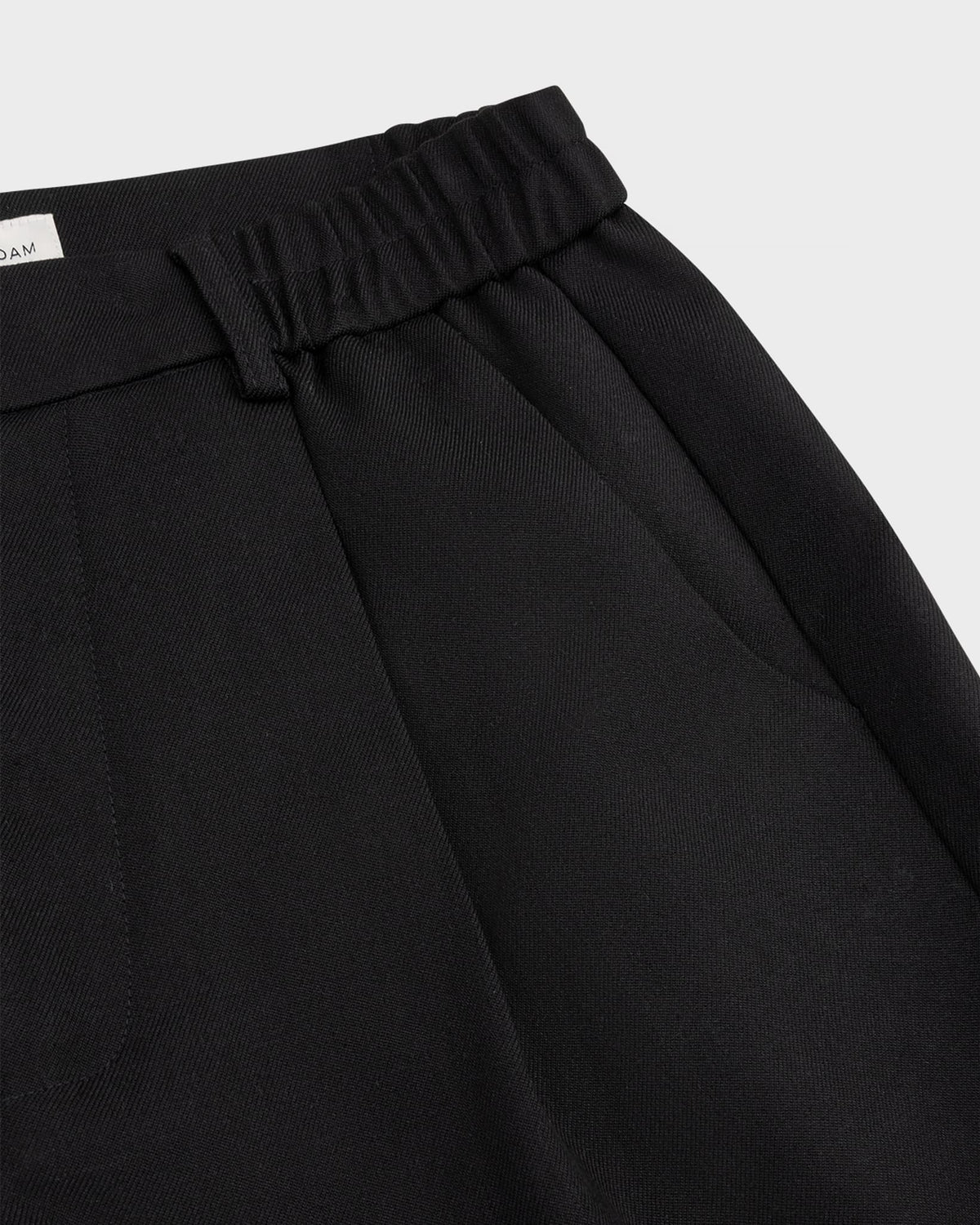 Close-up of the pleated elastic waistband and front pocket of black 264-15-1-3-20 trousers.